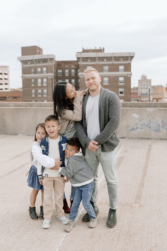 A family with three children poses on a rooftop in downtown Aurora, Illinois for their urban family photos taken by Charity White Photography