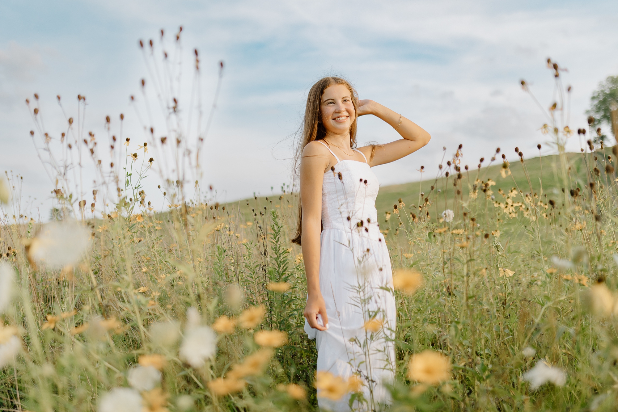 A girl in a white dress poses in a field of wildflowers for senior photos in Aurora Il at Oakhurst Forest Preserve.