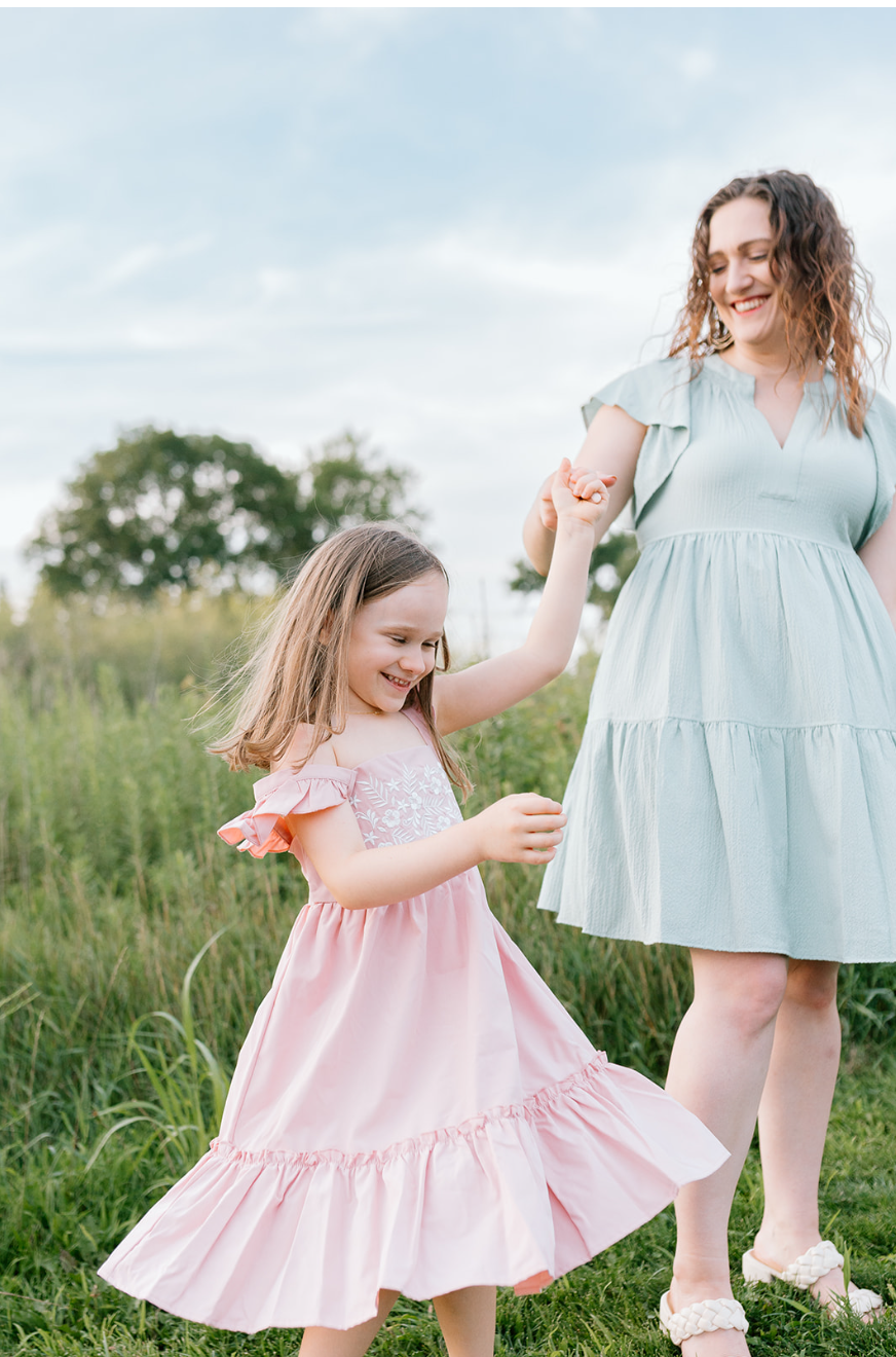 a girl in a pink dress is twirled by a woman in sage green dress