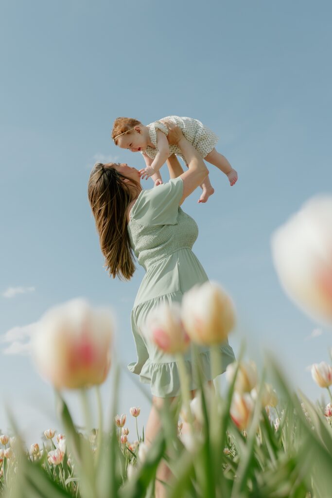 Mom tossing her baby in the air with colorful tulips blurred in the foreground.
