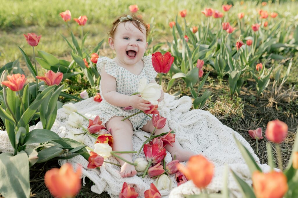 Baby sitting by herself directly in a field of colorful tulip petals.